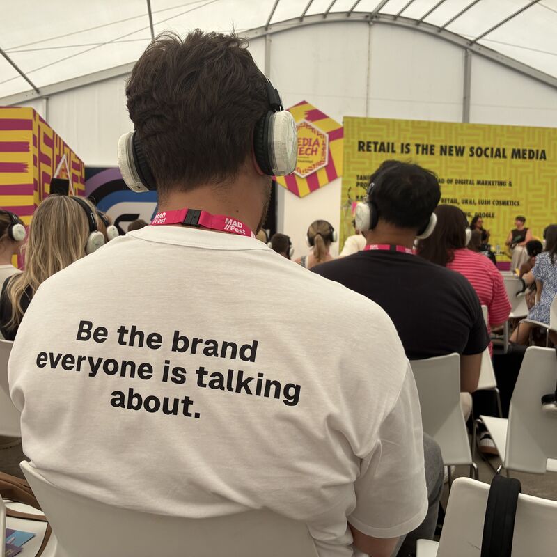 A man in headphones wears a t-shirt that reads on the back, "Be the brand everyone is talking about".