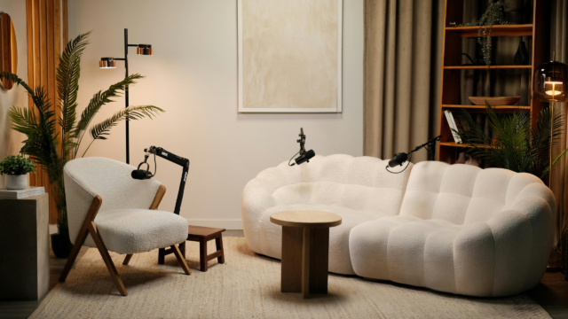 Modern podcast studio with three microphones arranged around a white armchair and curved sofa.