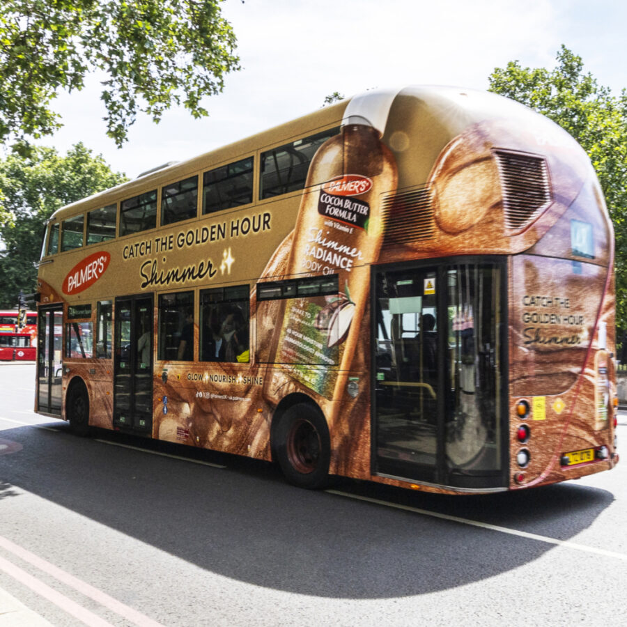 A London city double-decker bus wrapped in Palmer’s “Catch the Golden Hour” shimmer skincare ad.