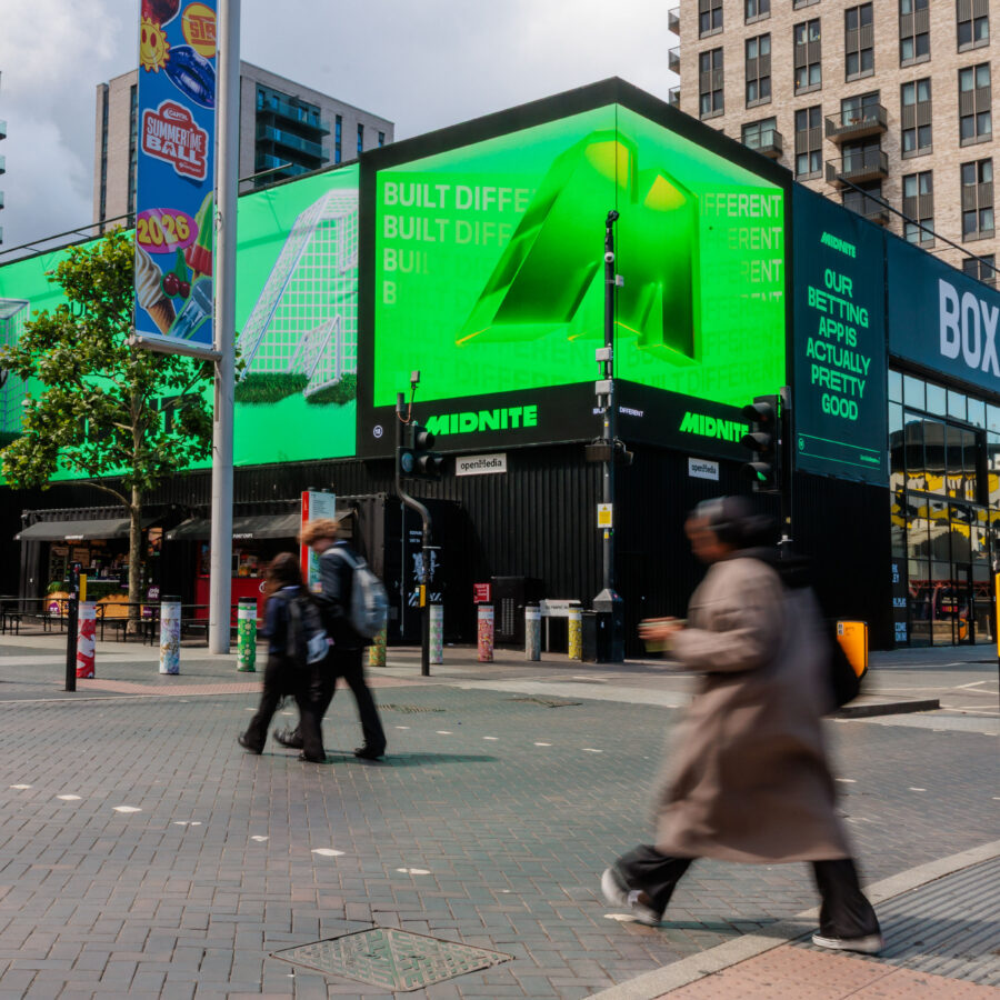 A vivid green Midnite billboard wraps the Wembley BOXPARK corner building, with glowing 3D geometric graphics and text; pedestrians blur past, creating a busy urban feel.