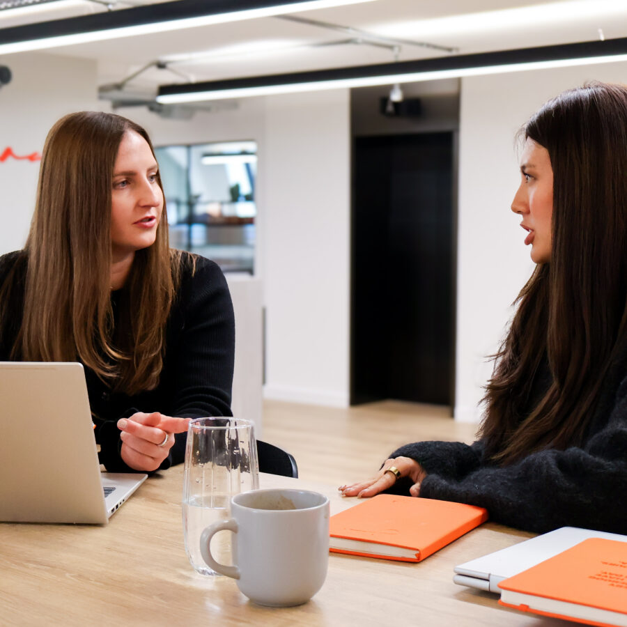 JAA team members talk over a coffee with orange notebooks and laptop open