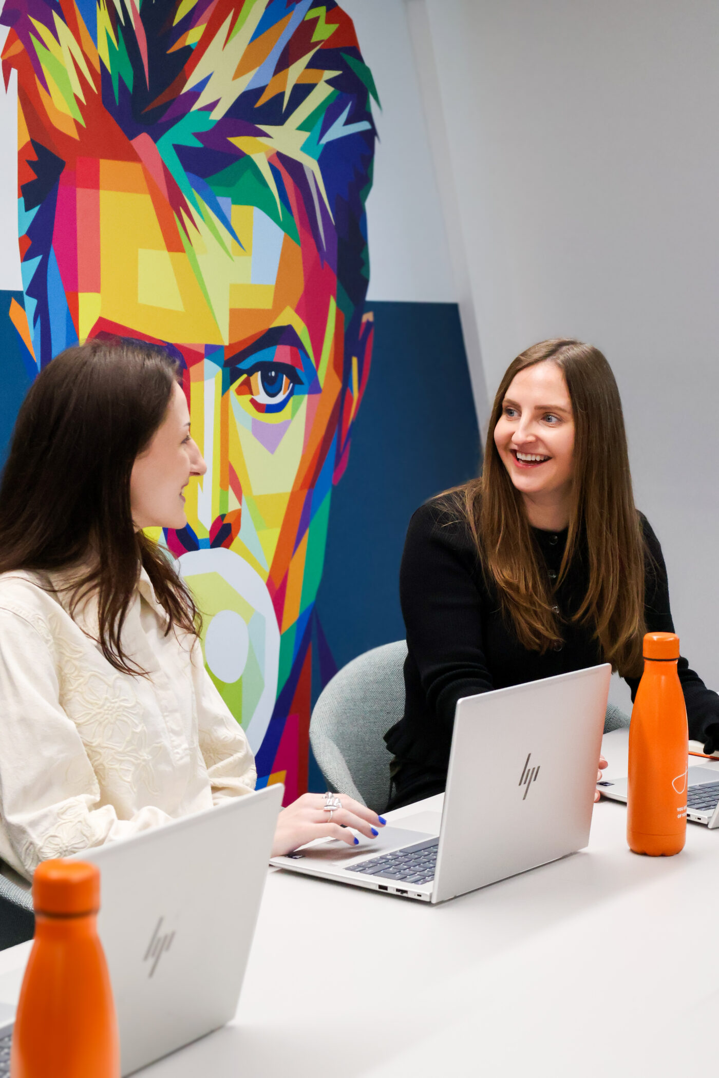 Two female colleagues chat in a meeting room