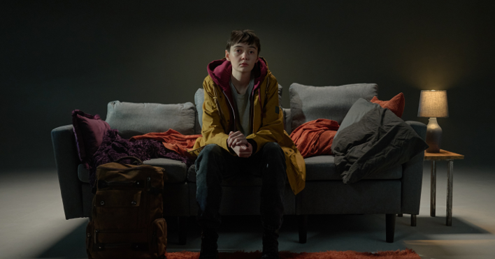A young person sits on a dark sofa