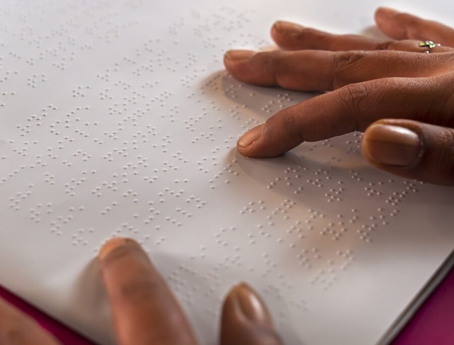 Fingers trace raised Braille dots on a white page, showing a visually impaired person reading by touch in a quiet, focused moment.