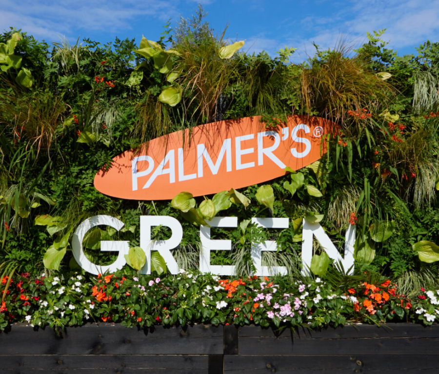 A Palmer's branded takeover of Palmer's Green tube station in London, showing the orange Palmer's logo amongstlush green foliage on the train platform.