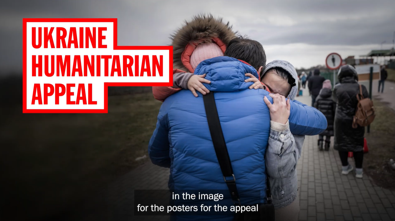 A family embraces on a grey Ukrainian street as people walk behind them; bold red-and-white text reads “Ukraine Humanitarian Appeal,” conveying grief and solidarity.
