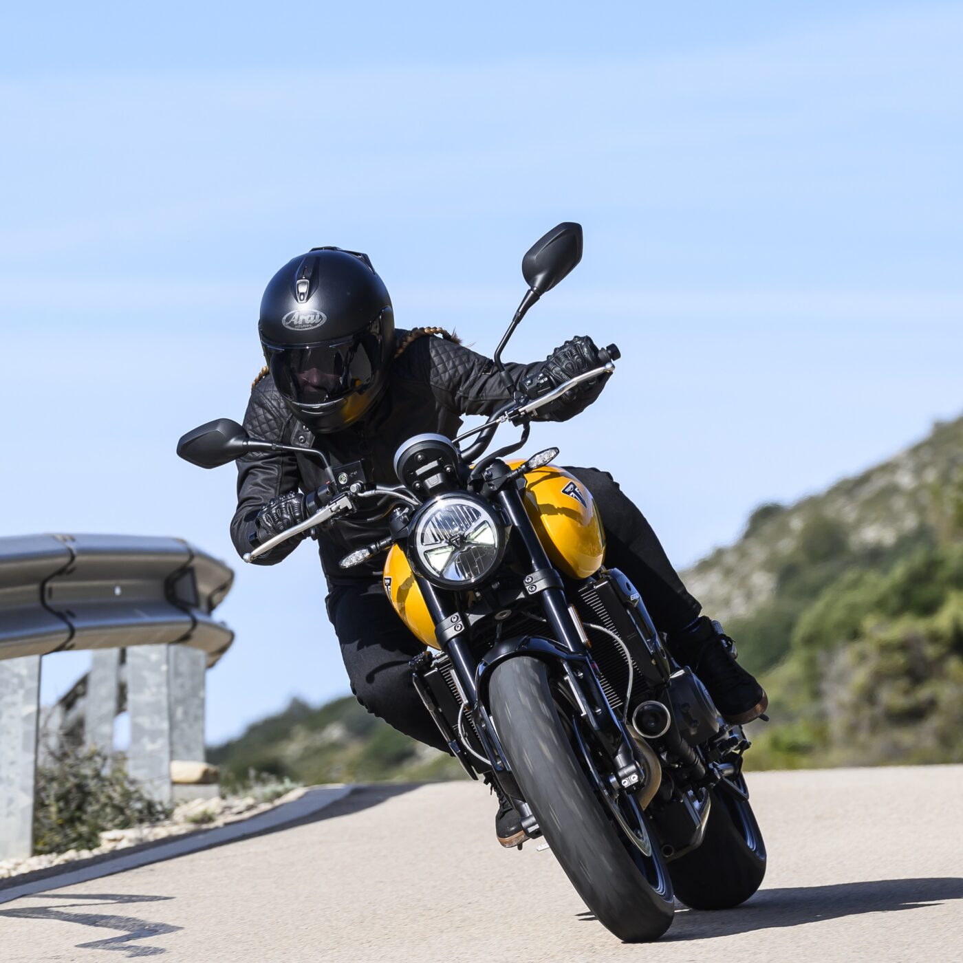 Triumph motorbike is being ridden by a leather clad rider leaning at an abgle with a blue sky behind