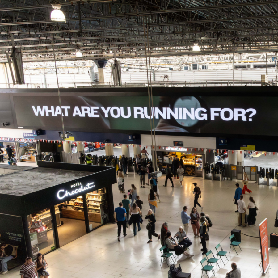 A busy train station hall with visitors browsing walking beneath a large Garmin digital ad reading “What are you running for?” This was on the day of the London Marathon.