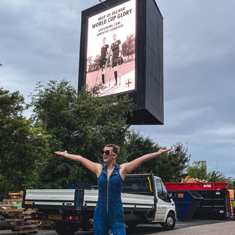 A team member from Amputee Lionesses is stood outside of billboard