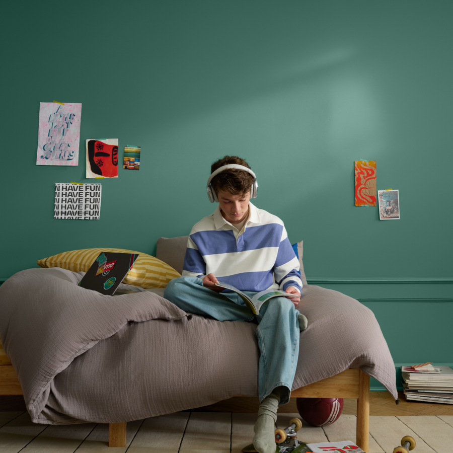 A boy is sitting on a bed drawing wearing headphones
