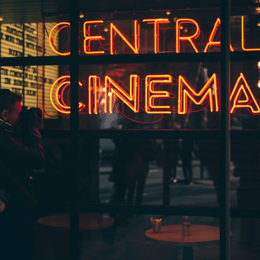 Orange neon lights reading 'Central Cinema' are reflected in a window on a dark evening
