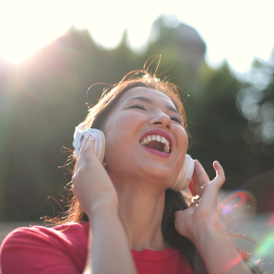 A woman is joyously listeing to music through her headphones as the sunshines behind her